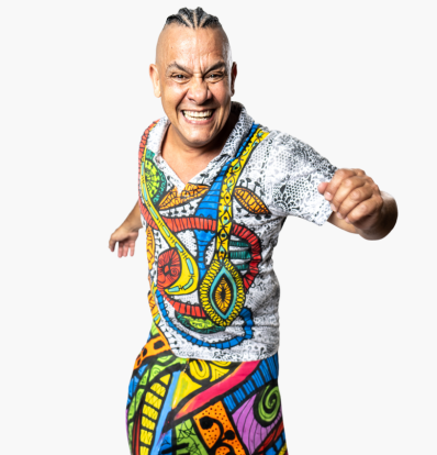 Sergio Xocolate dressed in traditional bright, multicoloured Brazilian clothing standing in a Capoeira pose with his arms half raised
