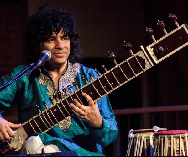 Anwar Kurshid plays the sitar, smiling, wearing bright blue