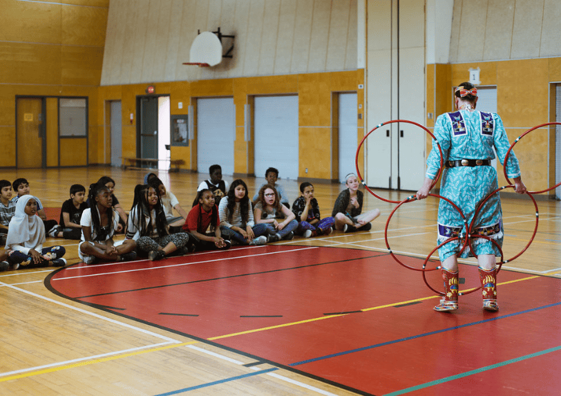 Naomi from Tribal Vision Dance demonstrates the hoop dance to students in a school gym