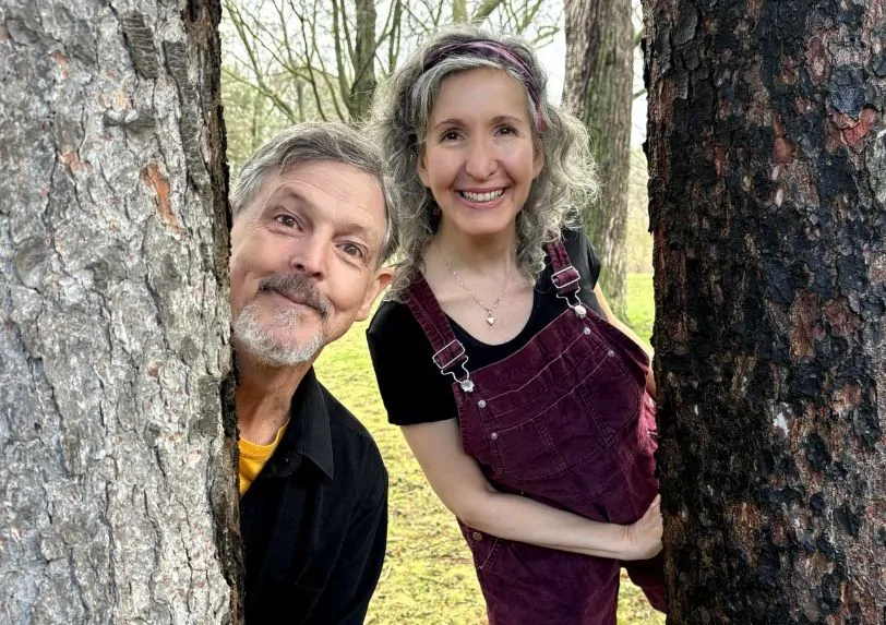 Two actors peak out from behind trees