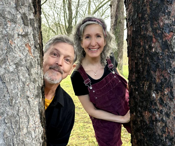 Two actors peak out from behind trees