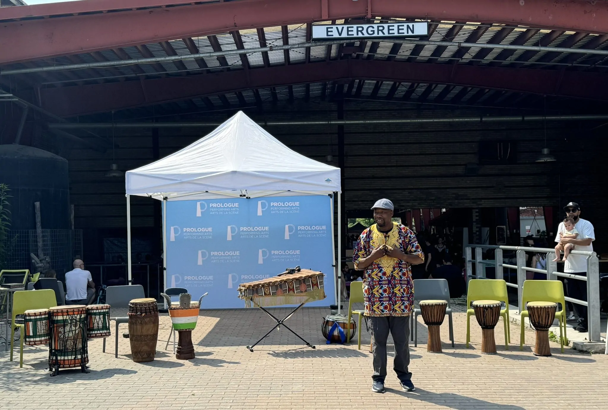 Fana Soro addresses the crowd at Arts Break at Brick Works. Behind him there are various percussion instruments which he will play throughout the show