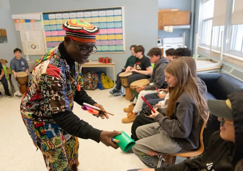 Nacko Backo hands a student a cowbell during a workshop
