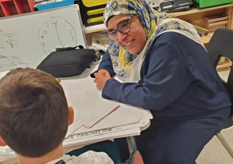Rukhsana sits at a desk with a student during the storytelling workshop